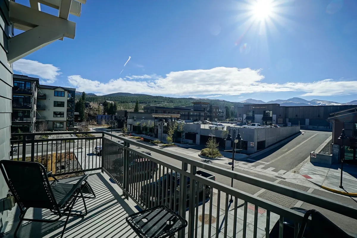 An exterior shot from a balcony with panoramic mountain views bathed in sunlight. The vantage point highlights the stunning natural surroundings, creating a sense of being immersed in the mountains while still enjoying the comforts of the property. The image quietly hints at morning coffee moments or post-adventure relaxation overlooking the landscape.