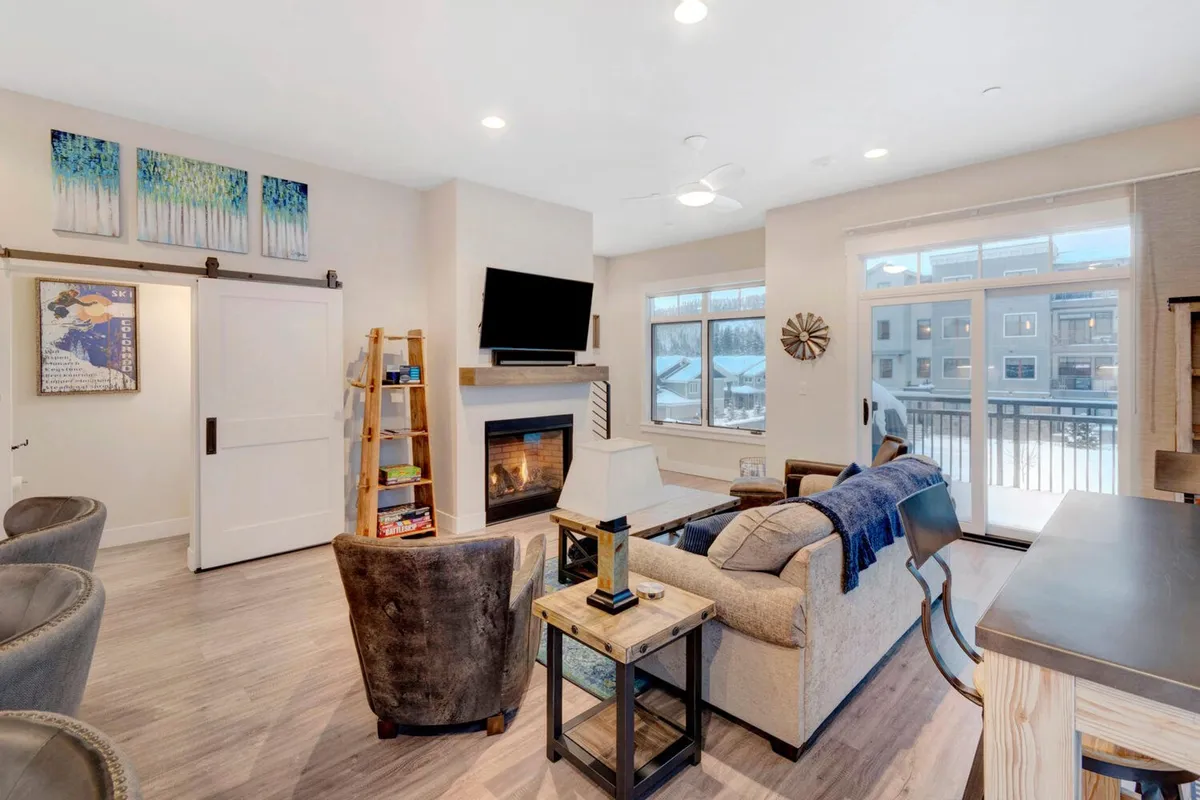 A cozy living area featuring a gas fireplace, plush sofa, large windows with a stunning view, and tasteful artwork. The mood is warm and welcoming, inviting guests to relax by the fire or host intimate gatherings while enjoying the mountain scenery.