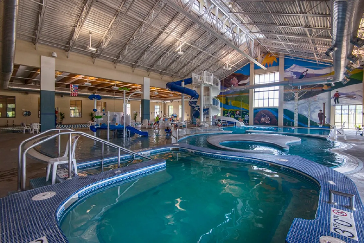 An indoor recreation center featuring a large pool with a water slide, play areas, and a colorful mural, creating a joyful, family-friendly atmosphere perfect for swimming and relaxing regardless of the season.