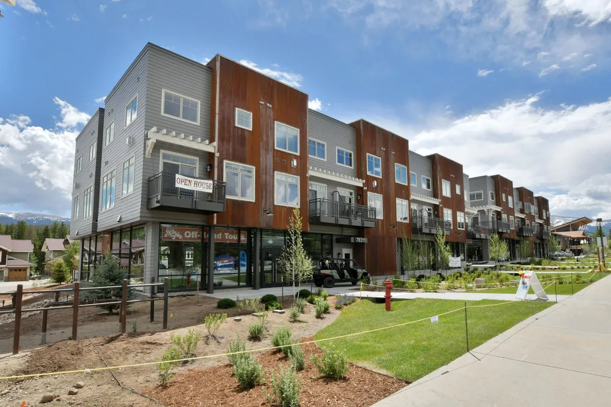 A modern exterior view of a mountain home, featuring clean architectural lines, landscaped grounds, and an inviting open house sign. The area is bathed in natural light, hinting at the vibrant neighborhood and easy access to outdoor amenities ideal for walks with pets.