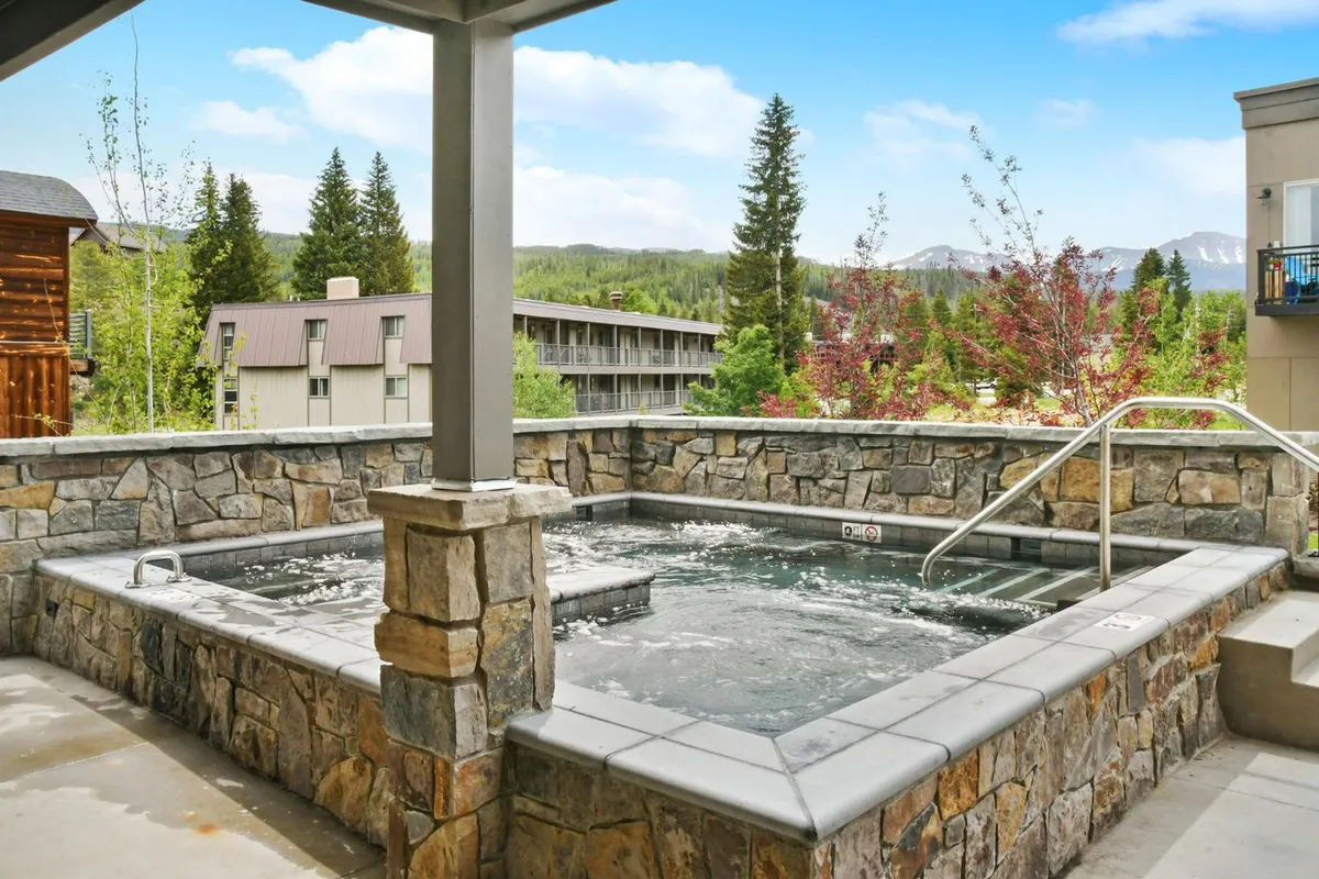 This image shows a serene and inviting hot tub area surrounded by natural stone walls and mountain views. A large, steaming hot tub sits at the center, inviting relaxation after an adventurous day. The lush natural surroundings and sunset lighting enhance the wellness and rejuvenation vibe.