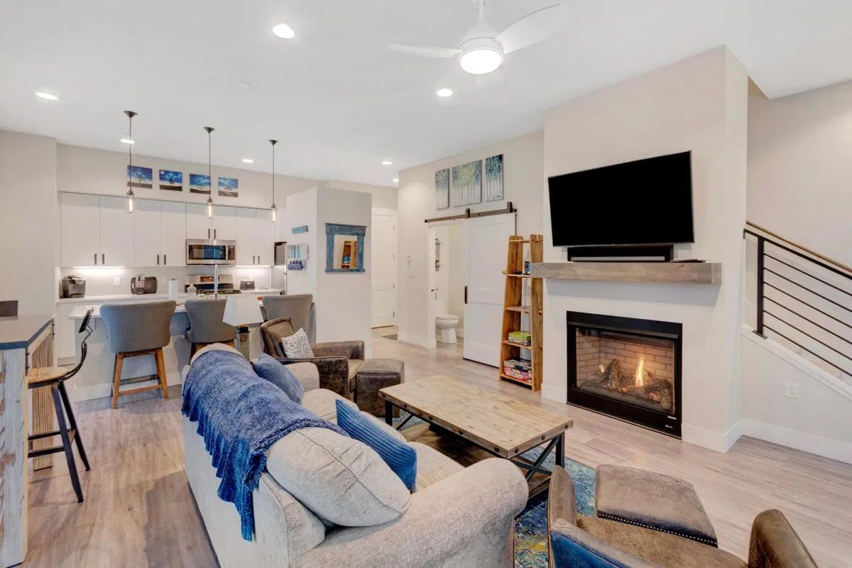 The image showcases the heart of the home: a warm, inviting living space with a glowing fireplace flanked by a plush sofa, an open kitchen island, and a spacious dining area, all designed for relaxation, social gatherings, and memorable meals.
