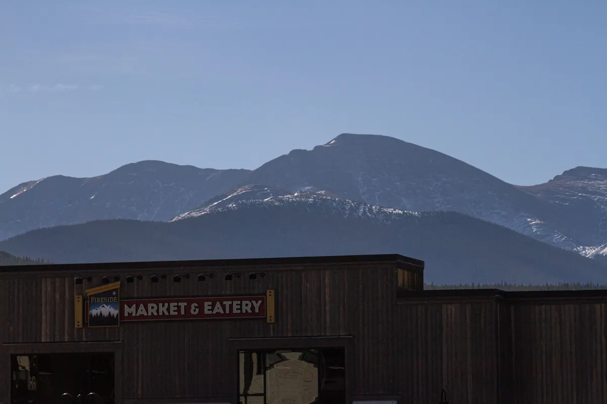A bustling community area with the 'Market & Eatery' sign in view, set against a scenic mountain backdrop. The patio area offers a space for gatherings, meals, and socializing with pets or family after outdoor adventures.