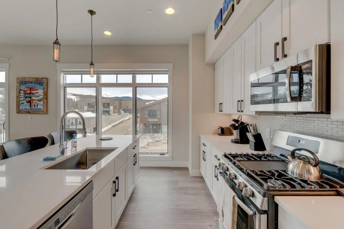 A modern chef's kitchen with a large island, stainless steel appliances, and expansive windows revealing a breathtaking mountain view. The space is warm and contemporary, designed for cooking and entertaining, with ample seating at the island for guests to gather.